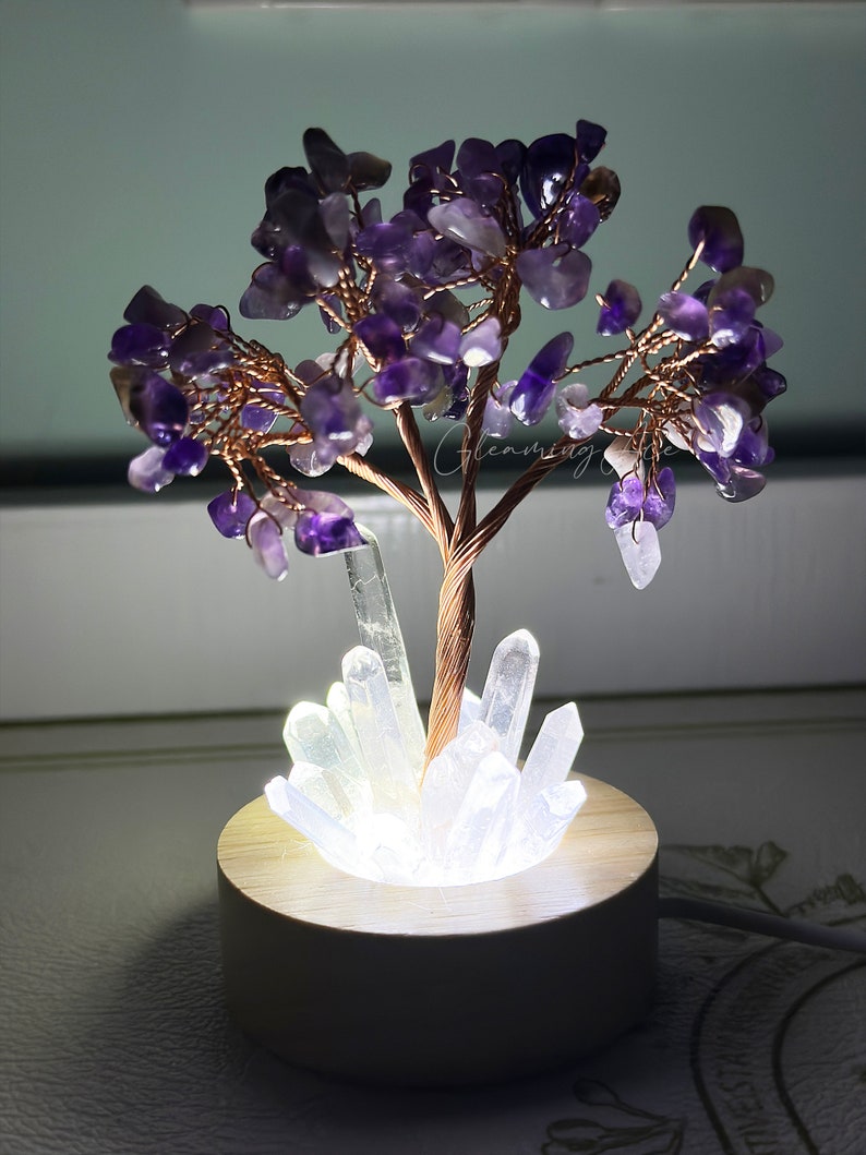 May include: Amethyst crystal tree with a white crystal base and a wooden stand with a built-in light. The tree is made of copper wire and amethyst crystals.