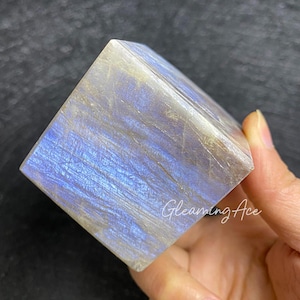 May include: A large, iridescent, cube-shaped labradorite crystal with a blue and white color scheme. The crystal is smooth and polished.
