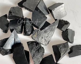 May include: A collection of black obsidian stones, some with a rough, jagged texture and others with a smoother, polished surface. The stones are arranged on a white background.
