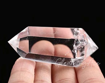 Könnte beinhalten: Ein klarer Quarzkristall mit doppelter Spitze, auch bekannt als Doppelendkristall, mit einer glatten, polierten Oberfläche. Der Kristall wird in einer Hand gehalten.