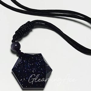 May include: A black necklace with a dark blue, star-shaped pendant. The pendant is made of a glittery material.