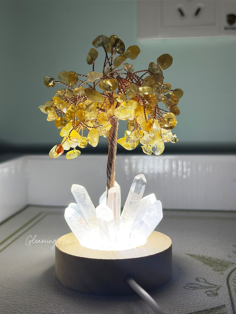 May include: A small crystal tree with a golden base and a light-up feature. The tree is made of clear quartz crystals and yellow citrine stones.