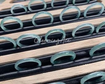 May include: A display of light green jade rings arranged on a wooden tray with black slots. The rings are smooth and translucent, with a subtle glow. The text "Gleaming Ace" is visible on the tray.
