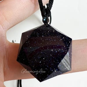 May include: A black necklace with a dark blue, hexagonal pendant. The pendant is made of a material that resembles a starry night sky.