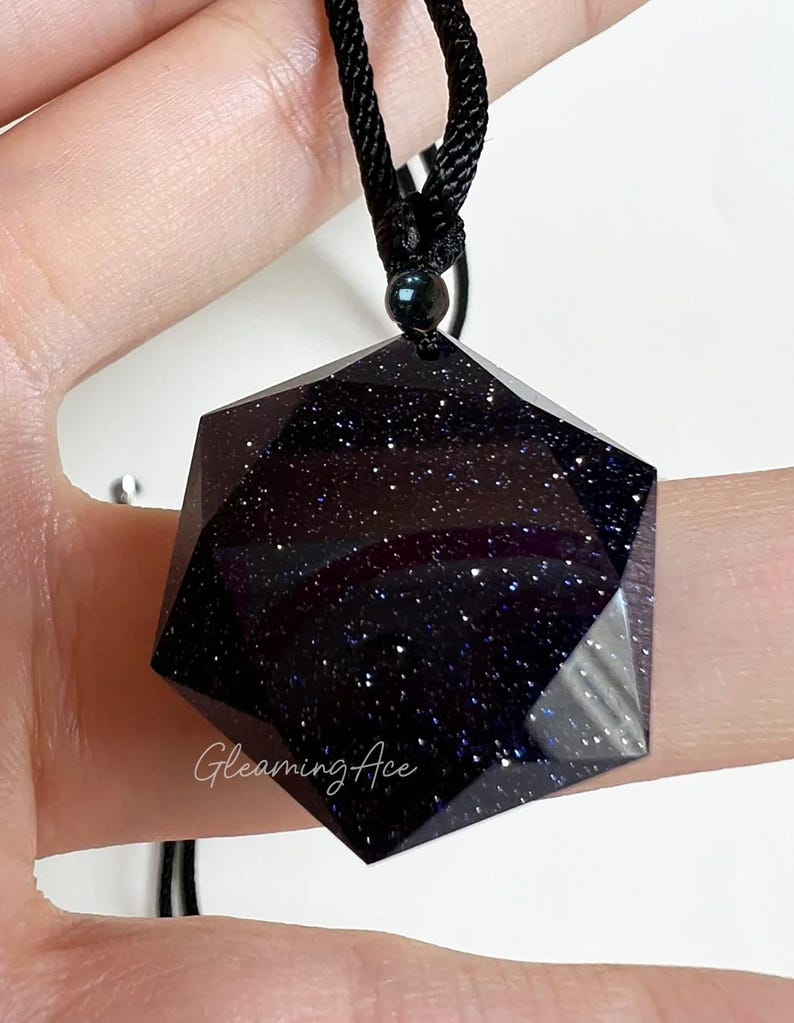 May include: A black necklace with a dark blue, hexagonal pendant. The pendant is made of a material that resembles a starry night sky.