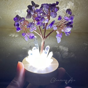 May include: A small amethyst crystal tree with a copper wire base and a white light base. The tree is lit up and the light shines through the crystals.