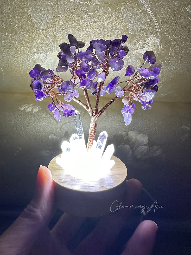 May include: A small amethyst crystal tree with a copper wire base and a white light base. The tree is lit up and the light shines through the crystals.