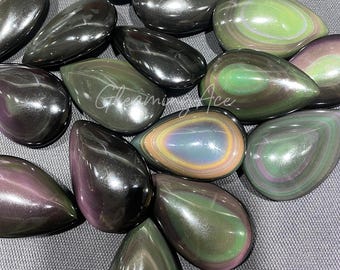 May include: A collection of polished obsidian teardrop-shaped stones. The stones display a range of colors, including black, green, purple, and iridescent hues. The surface of the stones is smooth and reflective, with a glossy finish.