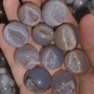 May include: A selection of spherical geodes in grey, lavender, and beige. Each geode is cut open to reveal a sparkling crystal interior. The text "Gleaming Ace" is visible on one of the geodes.