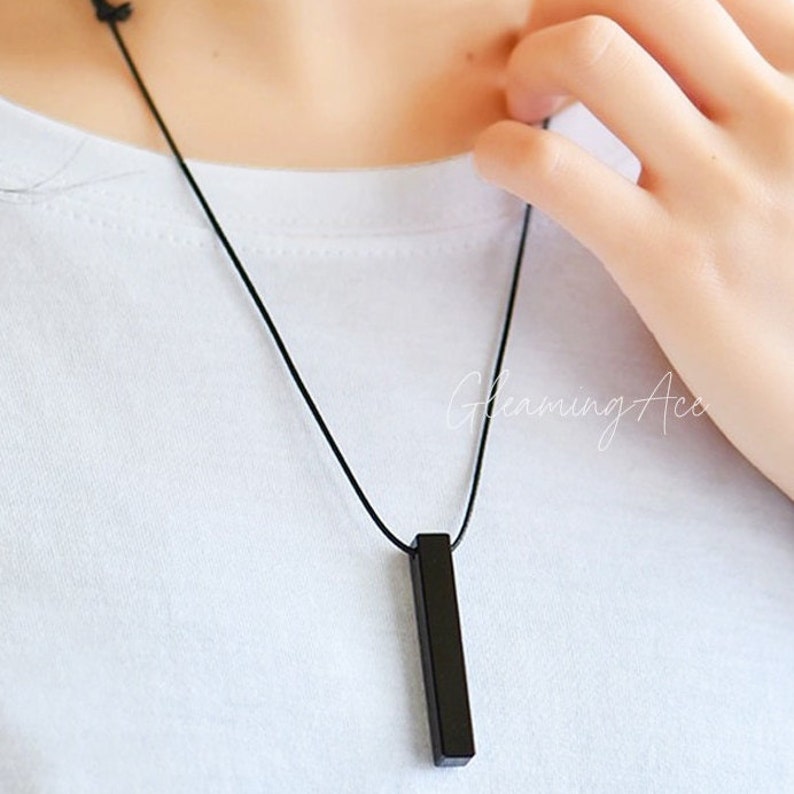 Puede incluir: Un collar negro con un colgante rectangular largo y delgado.