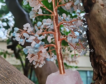 Pode incluir: Uma árvore de arame de cobre com pedras de cristal azuis e rosas. A árvore está sobre uma base de cristal rosa.