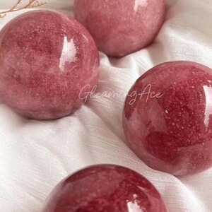 Peut inclure: Quatre sphères de verre rouges avec une finition scintillante. Les sphères sont disposées sur une surface en tissu blanc.