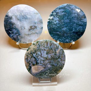 Puede incluir: Tres rodajas redondas de ágata, cada una con un patrón diferente de verde, azul y blanco. Las rodajas de ágata se muestran en pequeños soportes de metal.