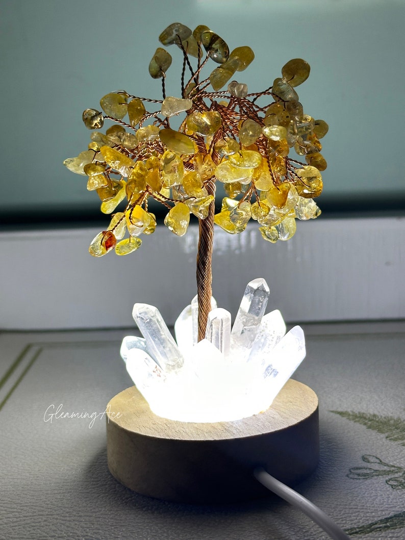 May include: A small, illuminated crystal tree with a golden base and a cluster of clear quartz crystals at the base. The tree is made of copper wire and yellow citrine stones.