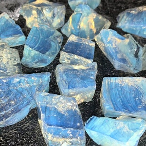 Könnte beinhalten: Eine Sammlung von blauen und weißen, irisierenden Glassteinen. Die Steine sind in verschiedenen Formen und Größen und haben ein durchscheinendes Aussehen.