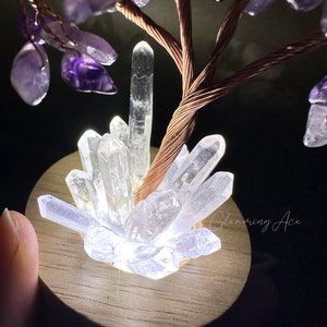 May include: A crystal tree with a copper wire base and amethyst crystals. The tree is lit from below, illuminating the clear quartz crystals at the base.