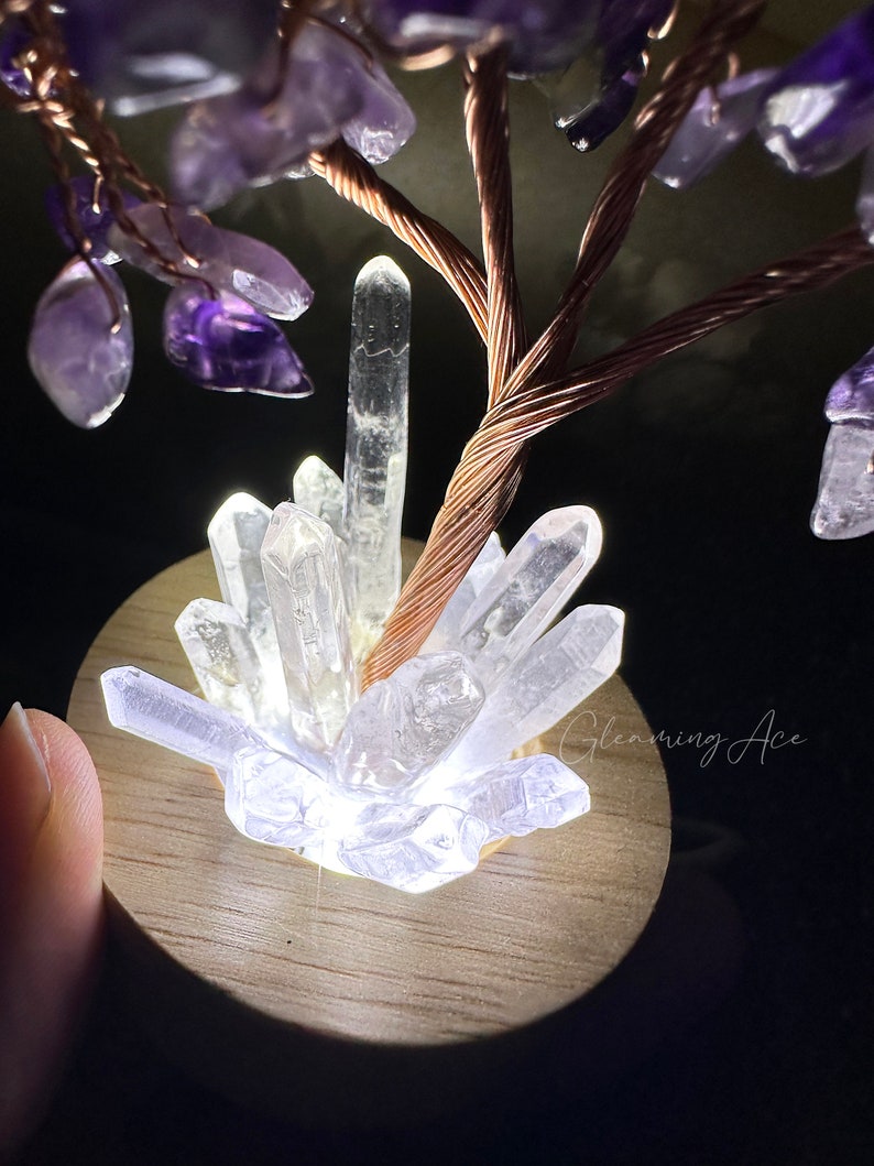May include: A crystal tree with a copper wire base and amethyst crystals. The tree is lit from below, illuminating the clear quartz crystals at the base.