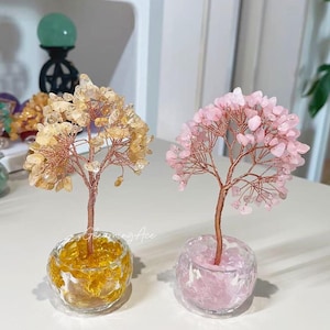 Könnte beinhalten: Zwei dekorative Kristallbäume. Einer hat gelbe Kristalle, der andere rosa. Beide haben Kupferdrahtzweige und braune Stämme, die in klaren Glasschalen stehen. Der gelbe Baum steht in einer gelb getönten Schale, der rosa in einer rosa getönten Schale.
