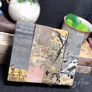 May include: Four rectangular slabs of polished stone with varying patterns of gray, black, gold, and pink. The slabs are arranged horizontally, side by side.