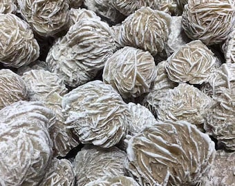 May include: A close-up of a pile of desert rose crystals. The crystals are a light brown color and have a rough, textured surface. They are arranged in a random pattern.