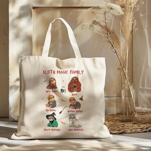 May include: A cream-colored tote bag with the text "SLOTH MAGIC FAMILY" and illustrations of sloths dressed as characters from a popular fantasy series. The bag has two white handles.