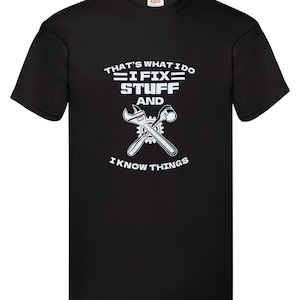May include: Black t-shirt with a white graphic featuring crossed wrenches and the text "THAT'S WHAT I DO, I FIX STUFF AND I KNOW THINGS". The shirt has a crew neck and short sleeves.