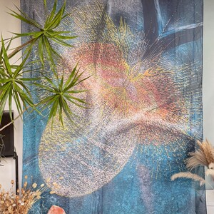 Op de afbeelding: Abstracte wanddecoratie met een blauw, oranje en geel ontwerp. Het kunstwerk heeft een textuurpatroon met een cirkelvorm. De afbeelding bevat ook planten en decoratieve items.