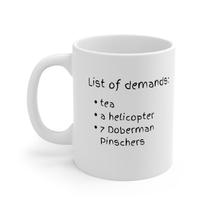 May include: White ceramic mug with black text that reads "List of demands: - tea - a helicopter - 7 Doberman Pinschers"