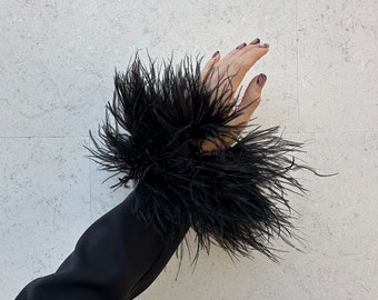 May include: A black long-sleeved shirt with a black feather cuff. The cuff is large and fluffy, and the feathers are arranged in a circular pattern.