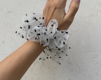 May include: White hair scrunchie with black polka dots. The scrunchie is made of a soft, sheer fabric.