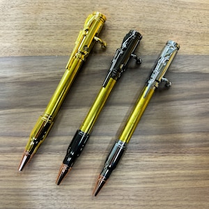 Peut inclure: Trois stylos dorés avec un design en forme de balle. Chaque stylo a une pointe de couleur différente : or, noir et argent.