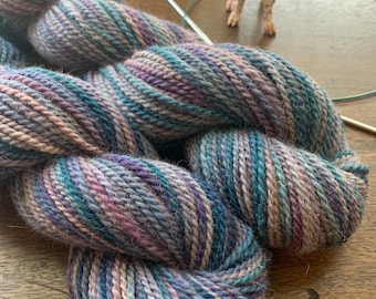 Puede incluir: Un ovillo de lana en una mezcla de colores azul, morado y rosa. La lana es suave y esponjosa, ideal para tejer o hacer ganchillo.