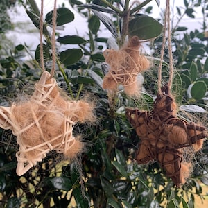 May include: Three handmade star ornaments made of woven twigs and natural fibers. The stars are hanging from twine and are a light brown, dark brown, and beige color.