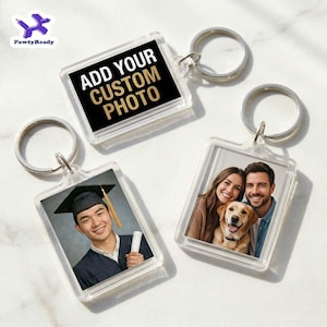 May include: Clear acrylic keychains with silver keyrings. One keychain has the text "ADD YOUR CUSTOM PHOTO" on a black background. Two keychains feature photos: a graduate in a cap and gown, and a couple with a dog.