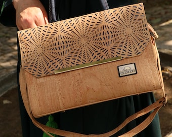 May include: A light brown cork handbag with a geometric design on the flap. The bag has a long, adjustable strap and a green tassel. The brand name "montado" is on a small label on the front.