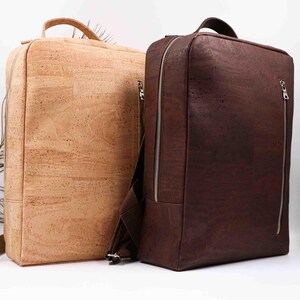Pode incluir: Duas mochilas de cortiça, uma castanha clara e outra castanha escura. Ambas têm formato retangular, uma alça superior e um zíper vertical. A mochila castanha escura tem um bolso frontal menor com zíper. As mochilas são feitas de material texturizado.