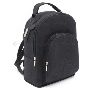 Pode incluir: Uma mochila preta de cortiça com um bolso frontal com zíper e uma alça superior. A mochila tem um puxador de zíper prateado e uma etiqueta prateada na alça.