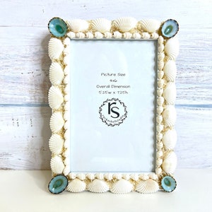 May include: White seashell picture frame with blue and green accents. The frame is decorated with seashells and has a 4x6 inch picture size. The overall dimension is 5.25 inches wide by 7.25 inches high.