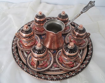 Pode incluir: Um conjunto de café turco de cobre com seis xícaras e pires, uma cafeteira e uma bandeja de servir. As xícaras e os pires são decorados com intrincados desenhos pintados à mão em tons de azul, vermelho e branco.