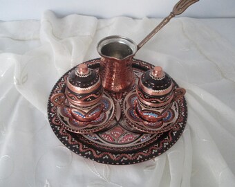 Pode incluir: Um conjunto tradicional de café turco com uma chaleira de cobre, duas xícaras e uma bandeja. O conjunto é decorado com intrincados desenhos pintados à mão em tons de azul, vermelho e branco.
