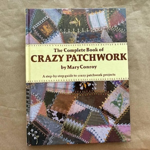 May include: A book titled "The Complete Book of Crazy Patchwork" by Mary Conroy. The cover features a colorful patchwork design with a variety of fabrics and textures.