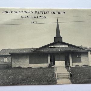 May include: Black and white photo of a church building with a steeple. The building is made of brick and has a sign that reads "First Southern Baptist Church". The photo was taken in 1971.