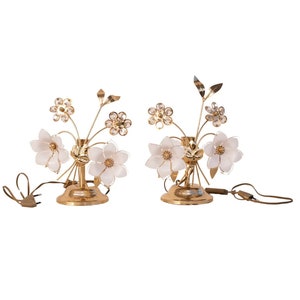 May include: A pair of gold table lamps with white flower-shaped shades and crystal accents. The lamps have a floral design and are perfect for adding a touch of elegance to any room.