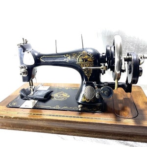 May include: Antique black sewing machine with gold accents and a wooden base. The machine has a hand crank and a needle plate.