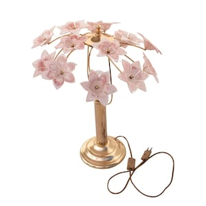 Può includere: Una lampada da tavolo dorata con un design floreale. Il paralume è fatto di fiori di vetro rosa.