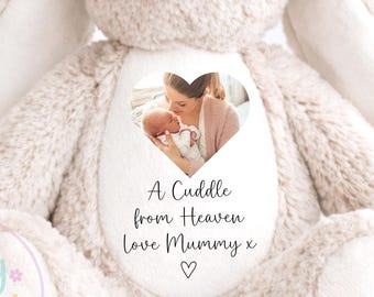 Pode incluir: Um coelho de pelúcia bege com olhos e nariz bordados. O coelho tem um patch em forma de coração com uma foto de uma mãe e um bebê. O texto no patch diz "A Cuddle from Heaven love Mummy x". Presente personalizado para crianças.