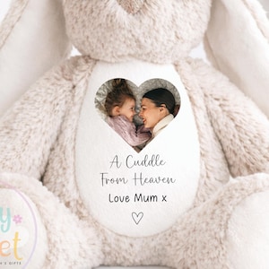 May include: A soft, beige plush bunny with embroidered eyes and nose. The bunny features a heart-shaped photo and the text "A Cuddle From Heaven, Love Mum x". The toy is designed to be safe for newborns. The bunny is a personalized children's gift.