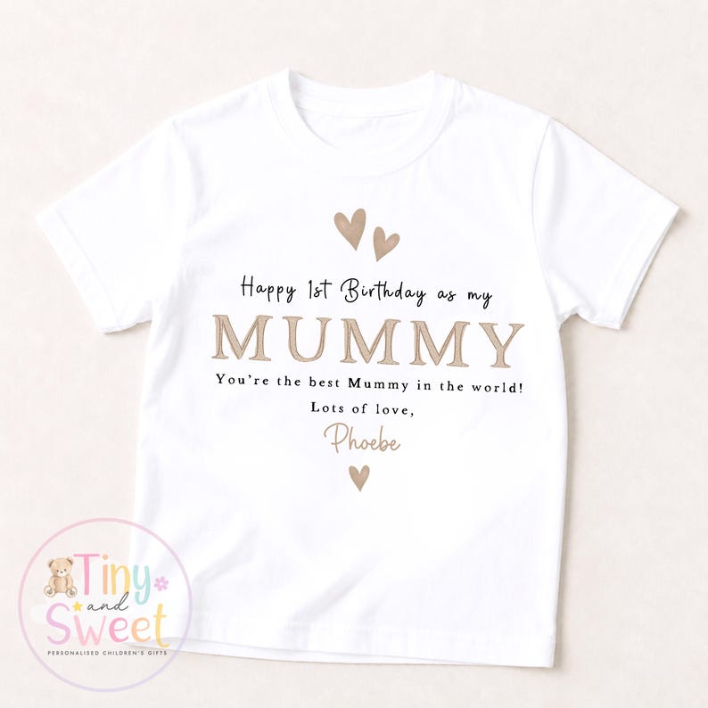 May include: A white short-sleeved t-shirt featuring the text "Happy 1st Birthday as my MUMMY. You're the best Mummy in the world! Lots of love, Phoebe" in black and tan lettering, accented with three small tan heart illustrations.