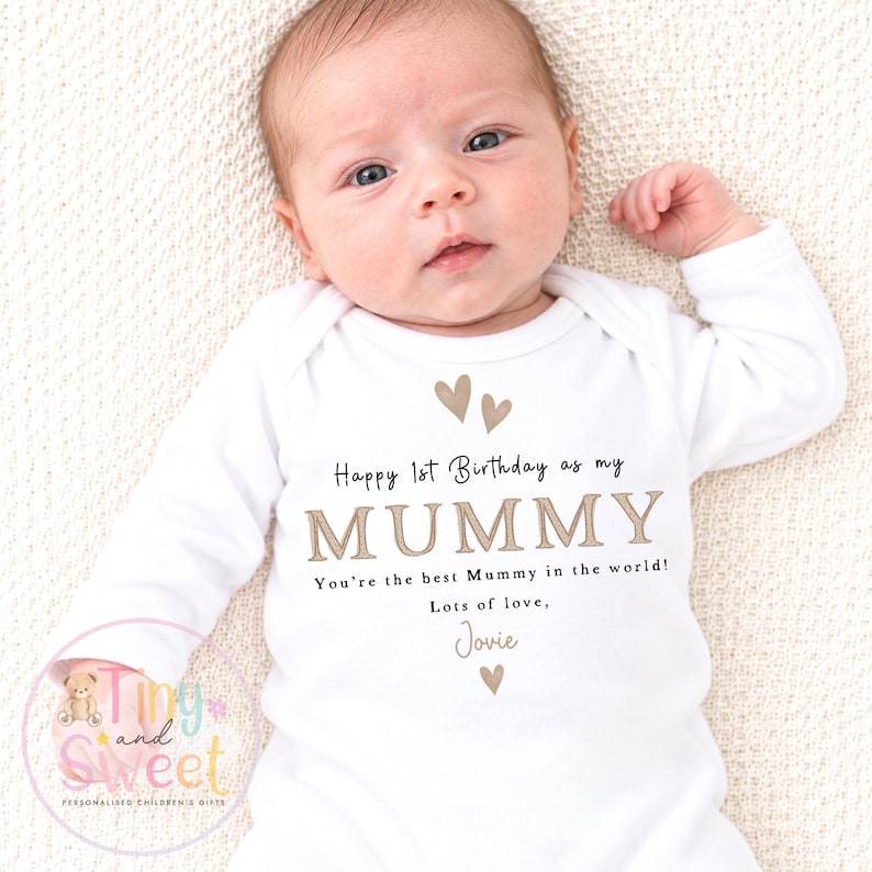 May include: A white long-sleeved baby bodysuit featuring the printed text Happy 1st Birthday as my MUMMY You're the best Mummy in the world! Lots of love, Jovie, accompanied by small brown heart icons centered on the chest area of the garment.