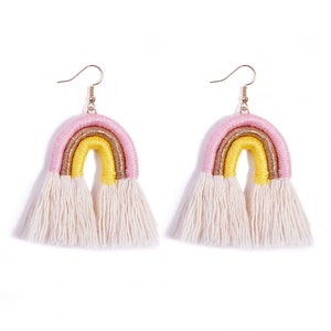 May include: A pair of rainbow-colored earrings with white fringe. The earrings are made of yarn and have a gold accent.